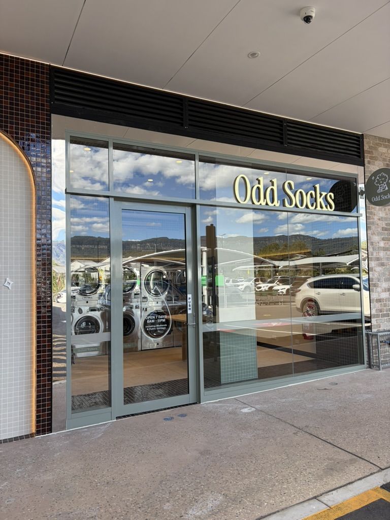 The Odd Socks entrance with sage green sliding doors and gold signage, machines visible through the glass.