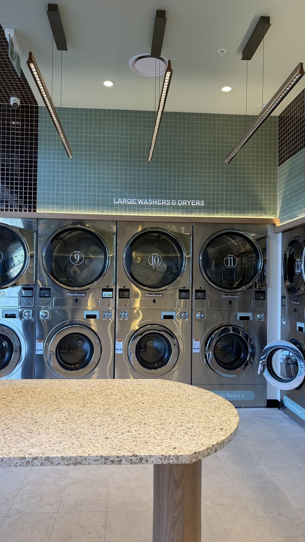 Inside Odd Socks: a terrazzo folding table in the foreground, with numbered large washers and dryers under sage green tiling behind it.