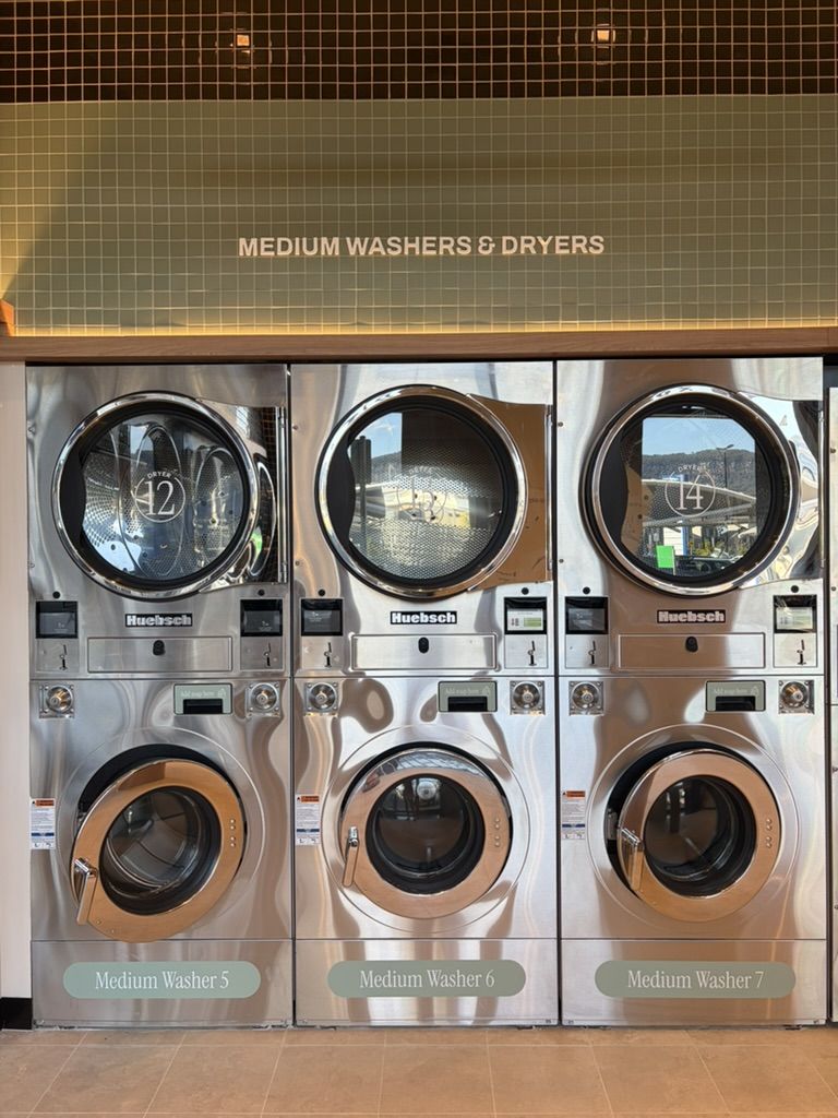 A bank of stacked Huebsch medium washers and dryers under tiled signage reading Medium Washers and Dryers.