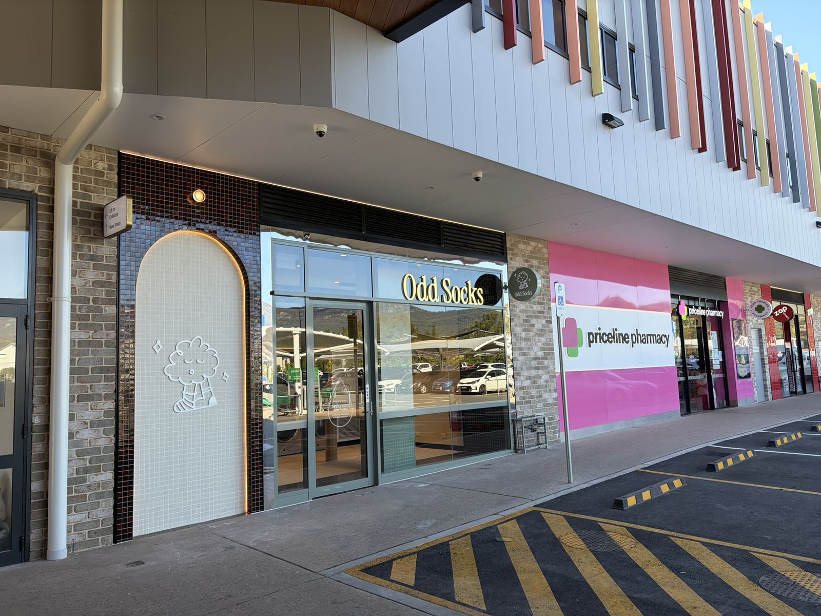 The Odd Socks shopfront at Calderwood Village, with gold lettering on glass and the escarpment reflected in the windows.